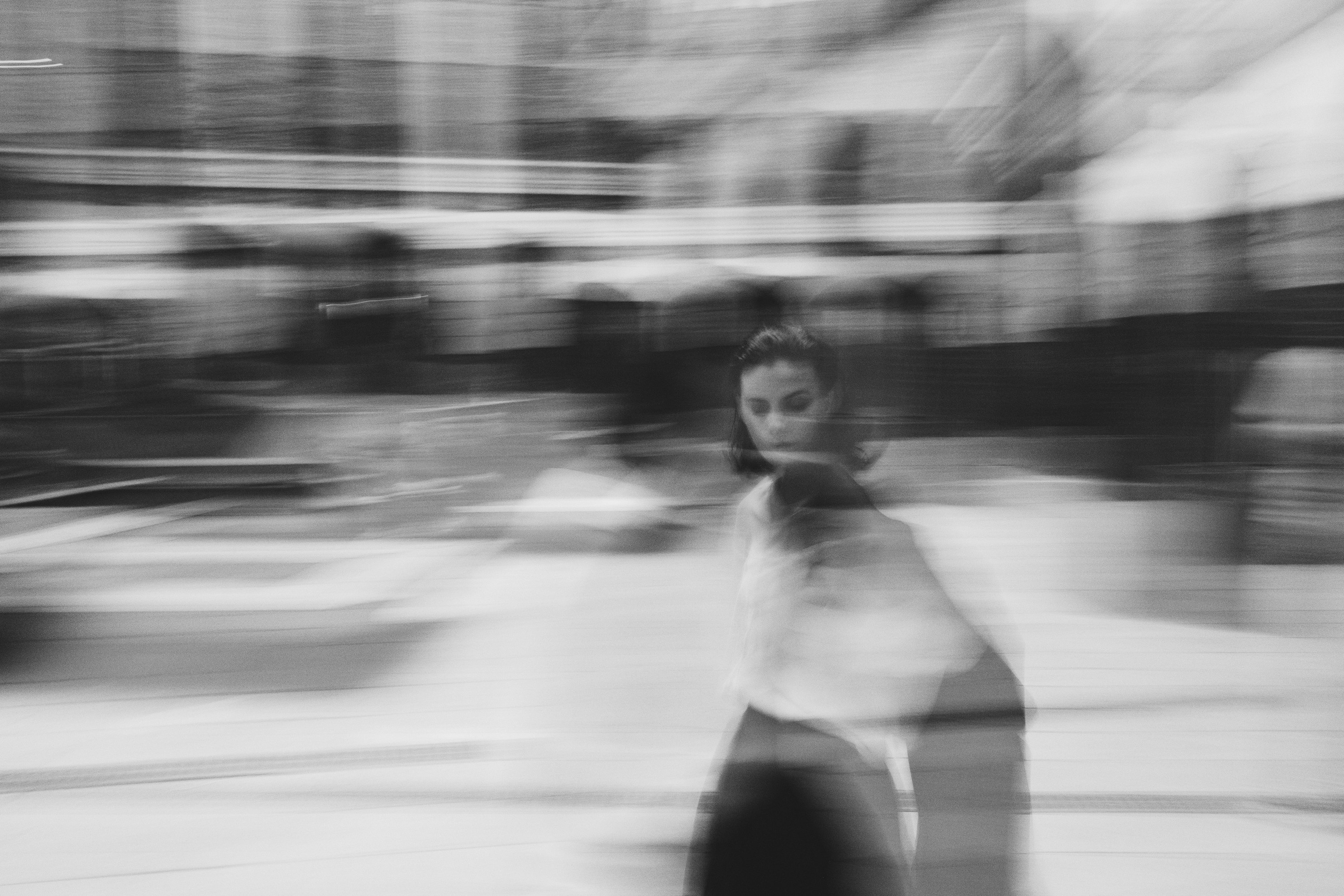 Blurred photo black and white photo and a women with shoulder length dark hair walking through a street